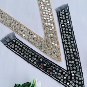 May include: Three decorative beaded trims in beige and black, adorned with small, round, reflective mirror-like embellishments. The trims are arranged on a white surface, with a few artificial flowers in the foreground.