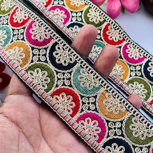 Peut inclure: Garniture brodée multicolore avec des motifs circulaires dans des tons de rouge, rose, vert, or et bleu. La garniture a un fond noir et des accents argentés et dorés.