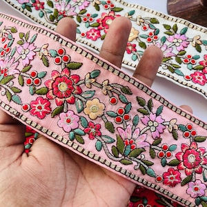 Peut inclure: Deux rubans de garniture brodés avec des motifs floraux. Le ruban du haut est blanc avec des fleurs roses et vertes. Le ruban du bas est rose avec des fleurs roses, vertes et rouges.