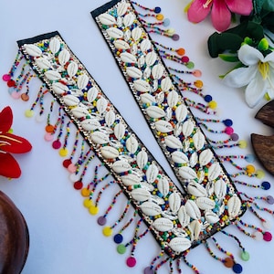 Op de afbeelding: Twee decoratieve zwarte stoffen stroken versierd met witte schelpen, kleurrijke kralen en pailletten. Elke strook heeft een kralenfranje in verschillende kleuren. Het ontwerp is ingewikkeld en opvallend, met een bohemien of kust esthetiek.