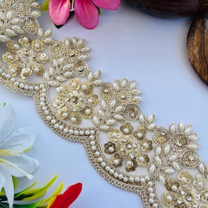 May include: Gold and ivory embroidered lace trim with floral and pearl accents. The trim has a scalloped edge and is embellished with sequins and small pearls. Ideal for embellishing garments or craft projects.