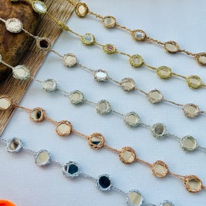 Op de afbeelding: Close-up van verschillende strengen decoratieve sierlijsten. Elke streng heeft kleine, ronde, spiegelende accenten, geweven in een metalen draad. De sierlijst is verkrijgbaar in goud, zilver en koper, geschikt voor het verfraaien van kleding of ambachten.