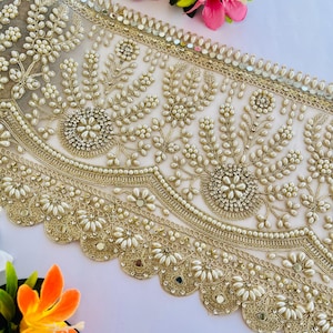 Pode incluir: Guarnição de renda bordada dourada com detalhes intrincados de flores e contas de pérolas. A guarnição apresenta uma borda ondulada e é adornada com pequenos espelhos. Ideal para embelezar roupas ou projetos de artesanato.