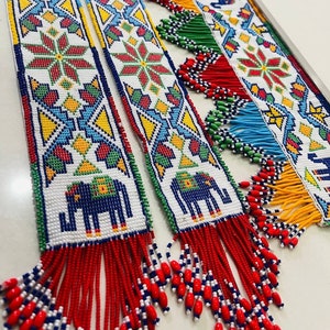 Puede incluir: Tres tapices de pared con cuentas con patrones geométricos coloridos y borlas. Los patrones incluyen elefantes, flores y formas geométricas. Las borlas son rojas, azules y amarillas.