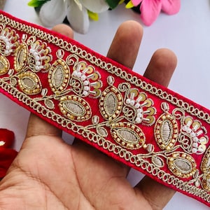 May include: A vibrant red embroidered trim with gold and white beadwork. The trim features an intricate floral design with gold thread and small white beads. This decorative trim is suitable for various craft projects.