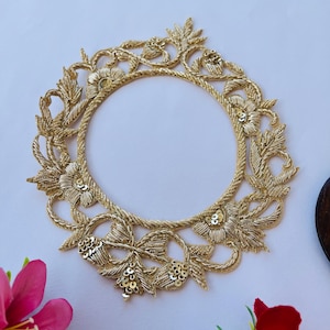 May include: Gold embroidered applique with a circular design featuring floral motifs and sequins. The applique is perfect for adding a touch of elegance to clothing or home decor projects.