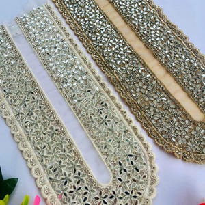 May include: Close-up of two decorative fabric trims. One is ivory with floral mirror embellishments and a scalloped edge. The other is gold with similar mirror accents. Both trims are designed for embellishing garments or crafts.