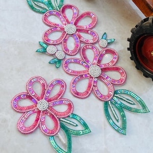 Peut inclure: Trois appliques de fleurs en sequins roses et verts avec des accents de perles. Les fleurs sont faites de sequins irisés et ont un design délicat et féminin.