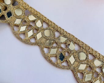 May include: Gold-colored decorative trim with reflective mirror accents. The trim features a scalloped edge and is embellished with round and diamond-shaped mirrors. The trim is likely used for embellishing clothing or craft projects.