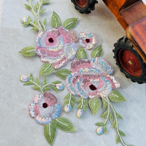 May include: A set of three pink and white floral appliques with iridescent sequins and green leaves. The appliques are made of fabric and are perfect for adding a touch of elegance to any project.