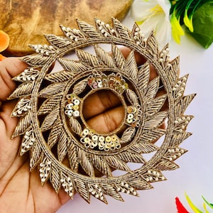 May include: A circular gold embroidered patch featuring a radiating leaf pattern with metallic thread, small white beads, and gold sequins arranged in a ring around the center. The design is intricate, with textured stitching and a hollow middle.