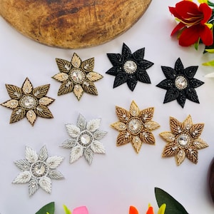 May include: An assortment of beaded star-shaped embellishments in various colors, including gold, silver, and black. Each star features a central clear rhinestone. These decorative elements are suitable for crafts and embellishments.