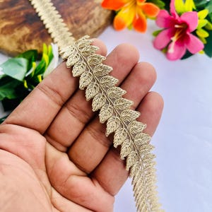 Peut inclure: Un ruban décoratif doré métallisé présentant un motif de feuilles répétitif. Le ruban est composé d'une tige centrale et de segments symétriques en forme de feuilles texturées, créant un design continu en forme de vigne pour l'ornement.