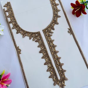 Peut inclure: Une applique en tissu brodé de couleur or avec un motif floral et de feuilles. L'applique a la forme d'un col et comprend des paillettes. L'applique est sur un fond blanc.