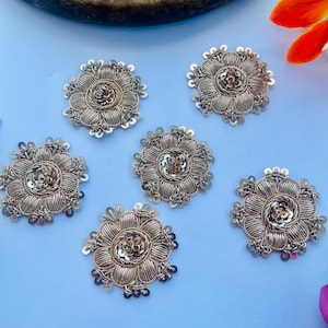 May include: Five circular metallic patches featuring a floral design. Each patch is crafted with silver-toned wire embroidery, radiating petals, and a central cluster of small metallic sequins. The edges are finished with tiny silver beads.