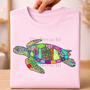May include: A light pink t-shirt featuring a large, colorful sea turtle graphic. The turtle's shell and body are composed of various vibrant, patterned segments including floral, geometric, and animal prints. The text TheDevachi is visible.