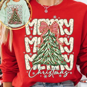 May include: A red crewneck sweatshirt featuring a large graphic of a green Christmas tree topped with a red and white checkered bow. The background text reads Merry Merry Christmas in a wavy font, accented with small snowflakes and ornaments.