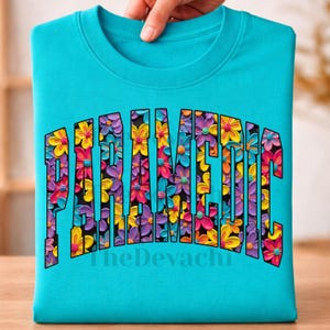 May include: A bright turquoise crew neck t-shirt featuring the word PARAMEDIC in large, bold, arched block letters. The interior of the letters is filled with a dense, colorful pattern of yellow, pink, purple, and blue flowers.