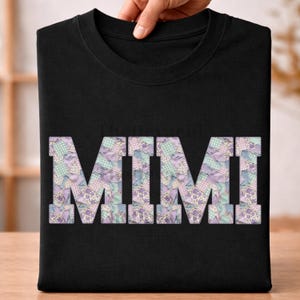 Może przedstawiać: Czarny t-shirt z okrągłym dekoltem z napisem "MIMI" w dużych literach w stylu patchwork. Litery wypełnione są pastelowymi wzorami kwiatowymi i w kratkę w odcieniach fioletu, zieleni i niebieskiego.
