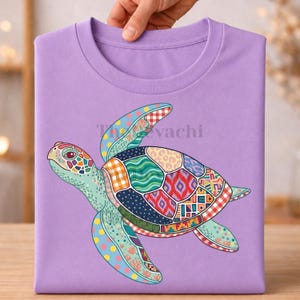 Könnte beinhalten: Ein hellviolettes T-Shirt mit einer großen, bunten Meeresschildkröten-Grafik. Der Panzer und die Flossen der Schildkröte sind mit einer Vielzahl lebendiger, mehrfarbiger geometrischer, floraler und tierischer Muster verziert. Der Text Thevachi ist sichtbar.
