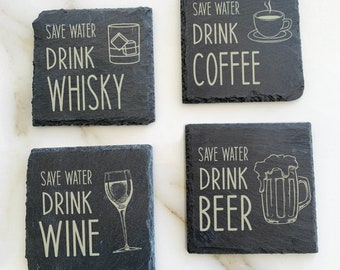 May include: Four black slate coasters with white text and images. The coasters say "Save Water Drink [Drink Name]" with a graphic of a glass of the drink. The drinks are whiskey, wine, coffee, and beer.
