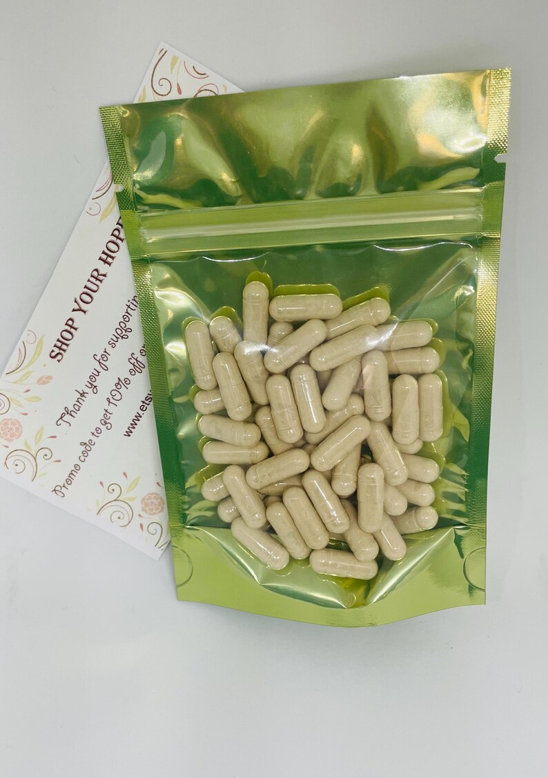 May include: A clear plastic bag filled with beige capsules. The bag is sealed with a gold-colored zipper and is set against a white background. A card with the text "SHOP YOUR HOP" is visible.