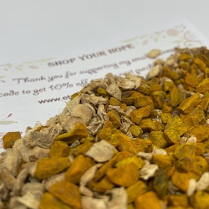 May include: Close-up of dried turmeric and ginger pieces. The turmeric has a vibrant yellow-orange color, while the ginger is a lighter tan. A white card with text that reads "SHOP YOUR HOPE" is partially visible in the background.