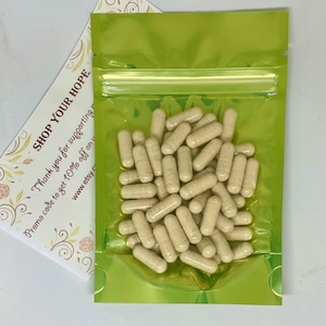 May include: A clear, lime green, resealable bag filled with beige capsules. A white card with the text "SHOP YOUR HOPE" and other text is visible behind the bag. The capsules are cylindrical and appear to be supplements.