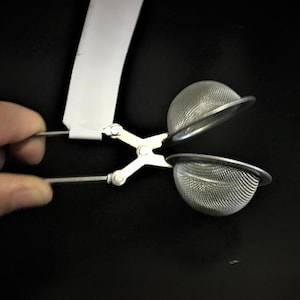 May include: A silver tea infuser with two mesh balls attached to a handle. The infuser is open and the balls are visible.