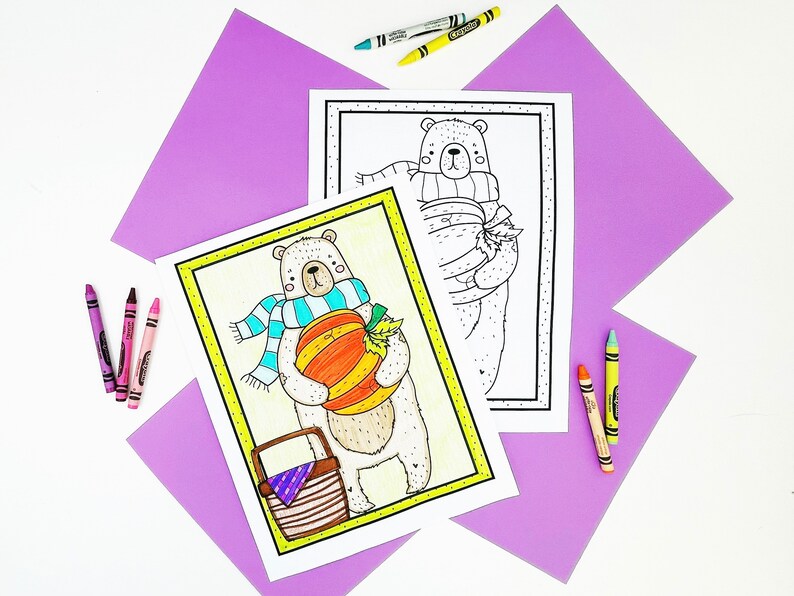 May include: Two coloring pages featuring cartoon bears, one colored and one outlined. The colored bear holds a pumpkin and wears a blue scarf. Crayons in various colors are scattered around the pages on a white surface with purple paper accents. The pages are framed in yellow.