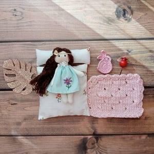 Handgemaakte minipop, miniatuurpop, wit bed met bloemen, kussen en roze wollen deken, roze konijn, bruin haar, 8,8 cm. hoog.