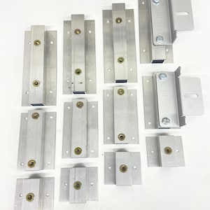 May include: An assortment of silver-colored metal brackets in various sizes, arranged on a white surface. The image includes text indicating the brackets are available in 2", 4", and 6" sizes, with multiple packs available. The brackets have a rectangular design with mounting holes.