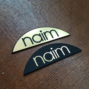 May include: Two half-circle nameplates, one gold and one black, with the word "naim" in white lettering.