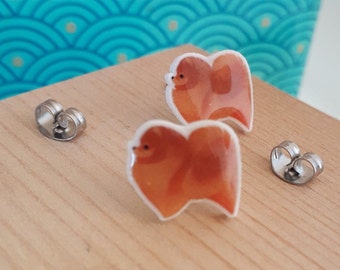 May include: A pair of stud earrings featuring a brown and white cartoon dog design. The earrings are made of metal and have a heart-shaped back.