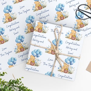 Puede incluir: Papel de regalo blanco con un patr&oacute;n repetido de Winnie de Pooh sosteniendo un tarro de miel con globos azules. El texto "Love The Taylors" y "Congratulations Ashley and Sean!" se repite en todo el patr&oacute;n.
