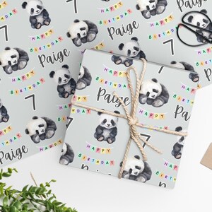 Op de afbeelding: Grijs inpakpapier met een herhalend patroon van aquarel-panda's, kleurrijke vlaggetjes en de tekst "Happy Birthday Paige" en het nummer "7".
