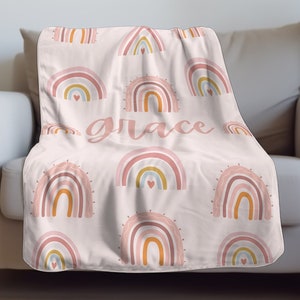 May include: A pink fleece throw blanket with a pattern of colorful rainbows and the word "grace" in a cursive font.