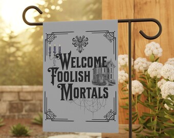 May include: A gray garden flag with a black and white illustration of a haunted house and the text "Welcome Foolish Mortals".