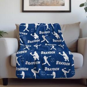May include: A blue fleece blanket with a white baseball player silhouette pattern. The blanket features the name "Brayden" repeated throughout the design.