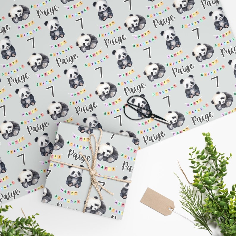 Op de afbeelding: Grijs inpakpapier met een herhalend patroon van aquarel-panda's, kleurrijke vlaggetjes en de tekst "Happy Birthday Paige" en het nummer "7".