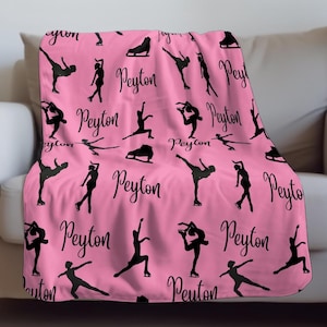 May include: A pink blanket featuring a pattern of black ice skating figures, ice skates, and the name "Peyton" in a cursive font. The blanket is draped over a white couch.