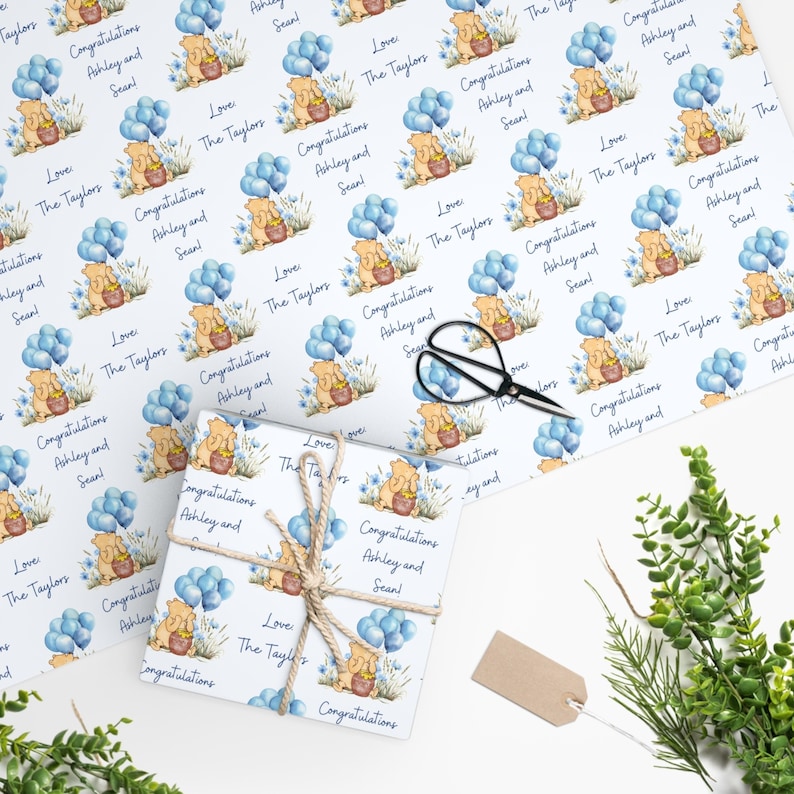 Puede incluir: Papel de regalo blanco con un patr&oacute;n repetido de Winnie de Pooh sosteniendo un tarro de miel con globos azules. El texto "Love The Taylors" y "Congratulations Ashley and Sean!" se repite en todo el patr&oacute;n.
