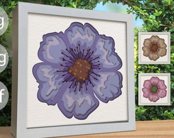 May include: A purple paper flower with a brown center, framed in a white frame. The flower is layered and has a 3D effect.