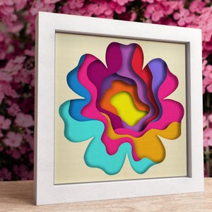 May include: A framed paper art piece featuring a colourful flower with layered petals in shades of blue, pink, orange, yellow, and purple.