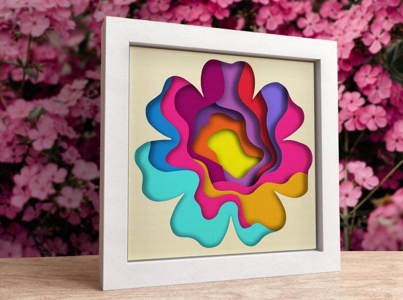 May include: A framed paper art piece featuring a colourful flower with layered petals in shades of blue, pink, orange, yellow, and purple.
