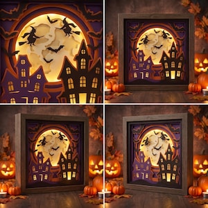 May include: A square shadow box featuring a layered paper cutout scene of a haunted house and witches flying on broomsticks against a large, illuminated full moon. The design uses purple and black silhouettes with warm yellow backlighting.