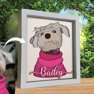 May include: A white dog with a pink sweater and the name "Bailey" written in pink cursive on a white canvas in a gray frame.