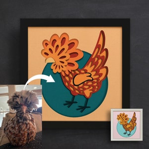 May include: A framed paper craft of a rooster with orange, red, and yellow feathers. The rooster is standing on a blue circle with a white outline. The frame is black with a white mat.