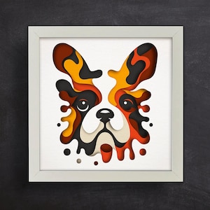 May include: A framed paper art piece depicting a stylized dog face. The artwork uses layered paper in shades of brown, orange, yellow, and black against a white background. The frame is white.
