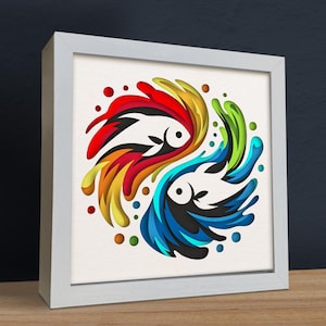 May include: A white framed wall art piece with a colorful paper cut design of two fish swimming in opposite directions. The fish are surrounded by swirls of red, orange, yellow, green, blue, and white.